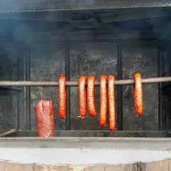 Wędzonka i kiełbasy wiszą w wędzarni, gotowe do parzenia wędlin po wędzeniu. Dym unosi się w powietrzu.