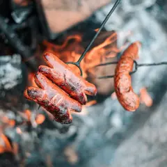 Kiełbaski pieką się nad ogniskiem. Dobre drewno na ognisko do kiełbasy to podstawa idealnego smaku.