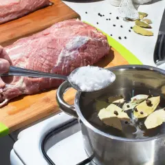 Jak uratować mięso z solanki? Dodaj sól do garnka z wodą, liśćmi laurowymi i pieprzem. Obok leży surowe mięso.