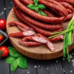Kabanosy na desce, z pomidorkami, szczypiorkiem i bazylią. Idealne, by zastanowić się, jakie przyprawy do kabanosów wybrać.
