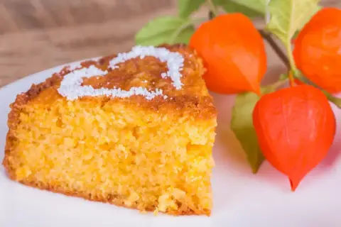 Szybkie ciasto z dyni przepis: wilgotny, pomarańczowy kawałek ciasta z cukrem pudrem w kształcie serca, ozdobiony pomarańczowymi miechunami.