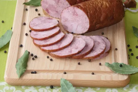 Kiełbasa szynkowa wędzona, pokrojona w plastry, na desce z pieprzem i liśćmi laurowymi. Idealna do domowego przepisu.