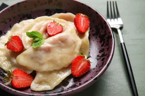 Pyszne pierogi z truskawkami, udekorowane świeżymi owocami i miętą, w ozdobnej misce.