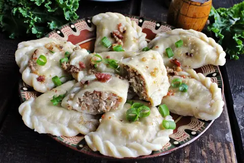 Pyszne pierogi z kaszą gryczaną, okraszone skwarkami i szczypiorkiem, na ozdobnym talerzu.