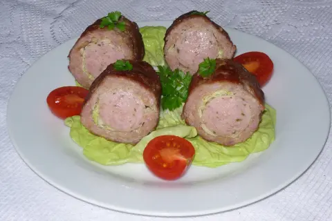 Cztery porcje grubej kiełbasy z mielonego mięsa, podane na sałacie z pomidorkami.