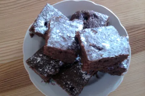 Czekoladowe ciasto z jednego jajka, pokrojone w kostkę i posypane cukrem pudrem, ułożone na talerzu.
