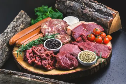 Mięsa, kiełbaski, pomidorki i przyprawy na drewnianej desce. Zastanawiasz się, ile cukru do solanki na wędliny?