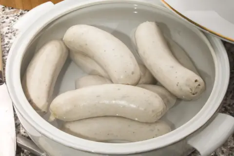 Biała kiełbasa w garnku, gotowa do parzenia. Delikatne, białe kiełbaski zanurzone w wodzie, czekają na idealny moment.