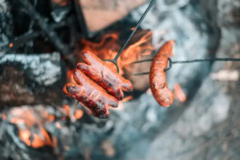 Kiełbaski pieką się nad ogniskiem. Dobre drewno na ognisko do kiełbasy to podstawa idealnego smaku.
