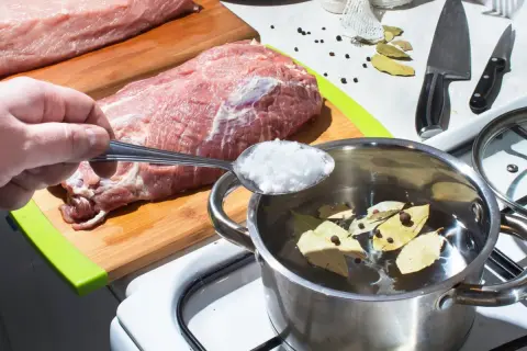 Przygotowanie solanki do schabu do wędzenia. Sól z łyżki trafia do garnka z wodą, liśćmi laurowymi i pieprzem.