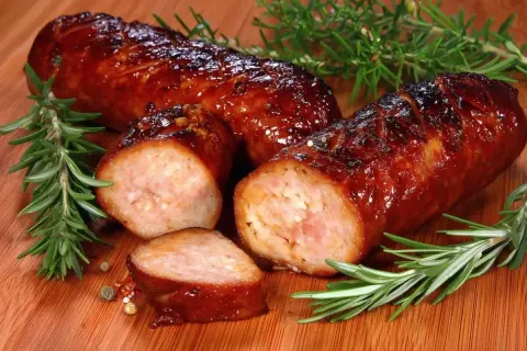 Soczysta kiełbasa z piekarnika, rumiana i aromatyczna, z gałązkami rozmarynu i ziarnami pieprzu.