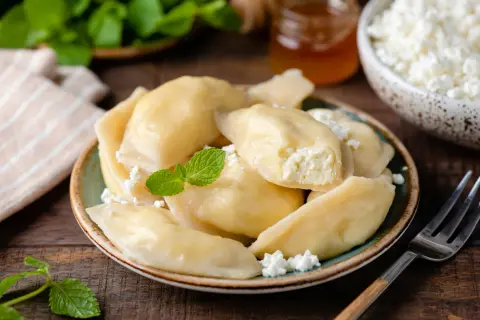 Pyszne pierogi z serem na słodko, udekorowane miętą i twarożkiem. Idealne na deser lub śniadanie.