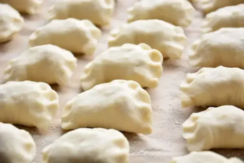 Gotowe do gotowania ciasto na pierogi ułożone rzędami na blacie.