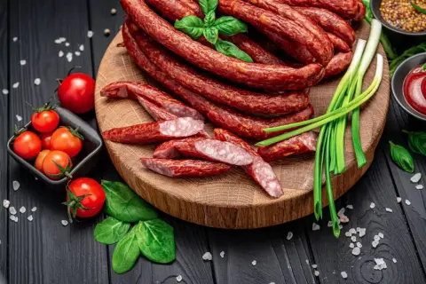 Kabanosy na desce, z pomidorkami, szczypiorkiem i bazylią. Idealne, by zastanowić się, jakie przyprawy do kabanosów wybrać.
