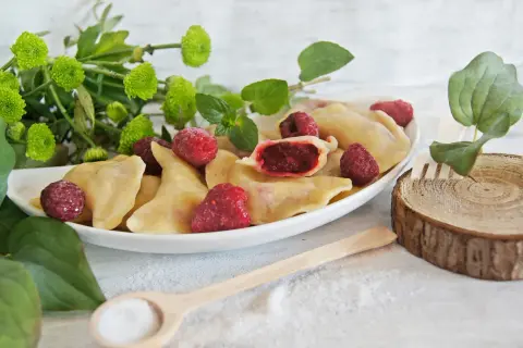 Pyszne pierogi z malinami, ozdobione świeżymi malinami i zielonymi listkami. Idealne na letni deser.