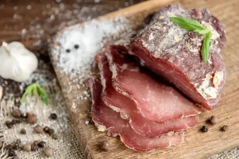 Pokrojone wędzone mięso na desce, obok czosnek i przyprawy. Idealne do peklowania mięsa przepis.