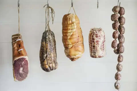 Wędzenie bez parzenia: wiszące szynki, salami i inne mięsne specjały, gotowe do dojrzewania.