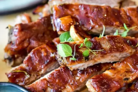 Soczyste żeberka w sosie barbecue, polane błyszczącym, ciemnym sosem, ozdobione świeżymi ziołami. Idealne na obiad.