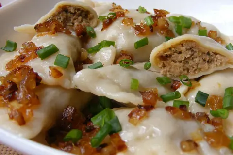 Pyszne pierogi z mięsem, posypane skwarkami i szczypiorkiem, kuszą swoim wyglądem.