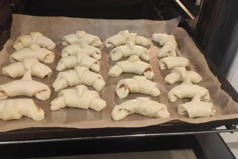 Gotowe do pieczenia rogaliki z marmoladą, ułożone na blasze wyłożonej papierem.