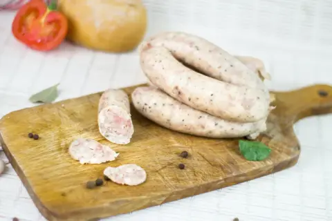 Biała kiełbasa na desce, obok pomidor, chleb i przyprawy. Zastanawiasz się, ile m mają jelita?