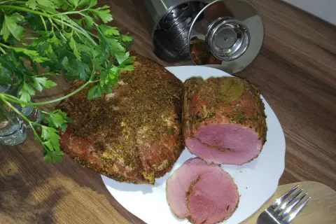 Schab w szynkowarze, przyprawiony i gotowy do krojenia. Obok świeża natka pietruszki i widelec.