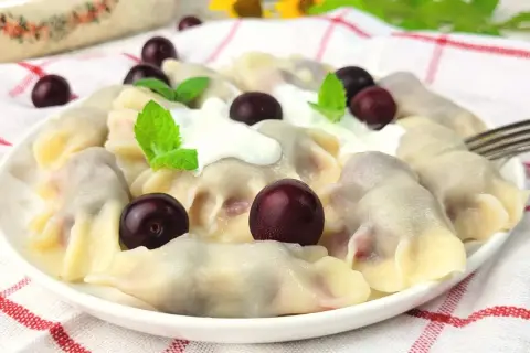 Pyszne pierogi z wiśniami, polane śmietaną i ozdobione świeżymi wiśniami i miętą. Letnia uczta na talerzu.