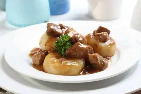 Pyszne kluski śląskie z gulaszem wołowym w sosie, udekorowane natką pietruszki.