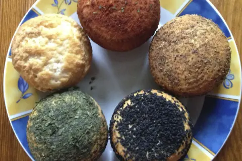 Pięć okrągłych serów na talerzu, jeden z czarnuszką, jeden z ziołami, jeden przypieczony, dwa naturalne. Idealne do przepisu na wędzony ser typu włoskiego.