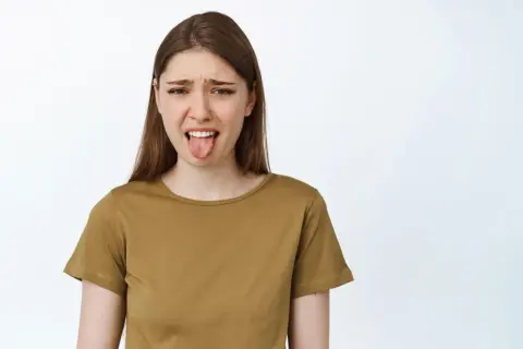 Dziewczyna z obrzydzeniem wyciąga język, jakby właśnie spróbowała kwaśnej kiełbasy po wędzeniu.