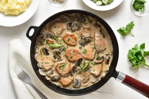 Soczyste polędwiczki w sosie pieczarkowym, podane w patelni, z gałązkami rozmarynu i posypane natką pietruszki. Obok puree ziemniaczane.