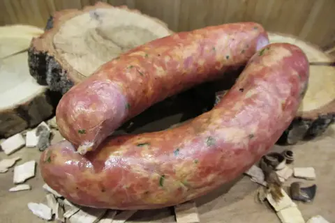 Dwie świeże kiełbasy, idealnie doprawione majerankiem, leżą na drewnianych plastrach.