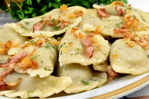 Talerz pełen pysznych, domowych pierogów z młodej kapusty, posypanych skwarkami i koperkiem.