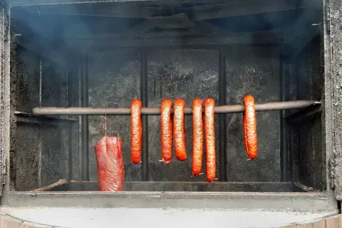 Wędzimy kiełbasę krok po kroku. Wędzone mięso i kiełbaski wiszą w wędzarni, nabierając aromatu dymu.