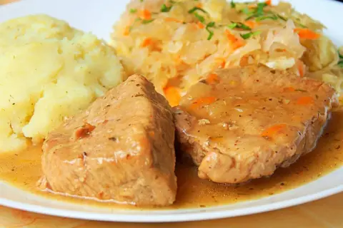 Soczysta pieczeń z szynki w sosie własnym, podana z purée ziemniaczanym i surówką z kiszonej kapusty. Pyszny, domowy obiad.