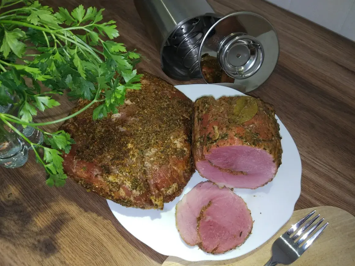 Schab w szynkowarze, przyprawiony i gotowy do krojenia. Obok świeża natka pietruszki i widelec.