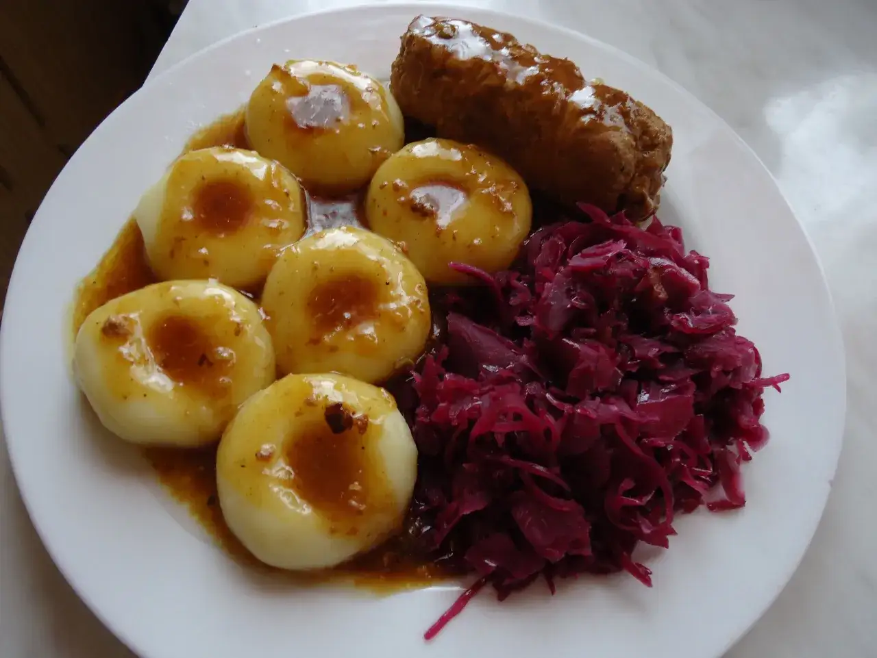 Pyszne kluski śląskie polane sosem, obok czerwona kapusta i kiełbaska. Tradycyjny polski obiad.