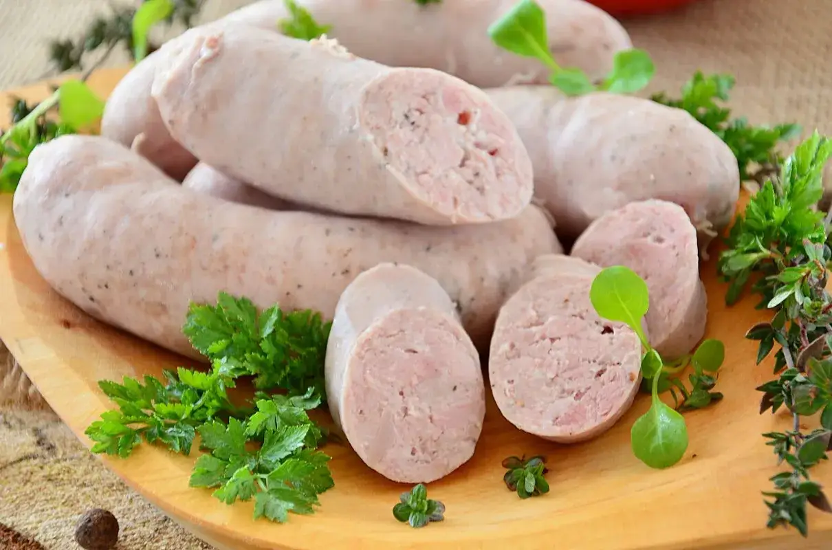 Biała kiełbasa na desce, z ziołami. Ile soli do białej kiełbasy? Idealna proporcja to klucz do smaku.