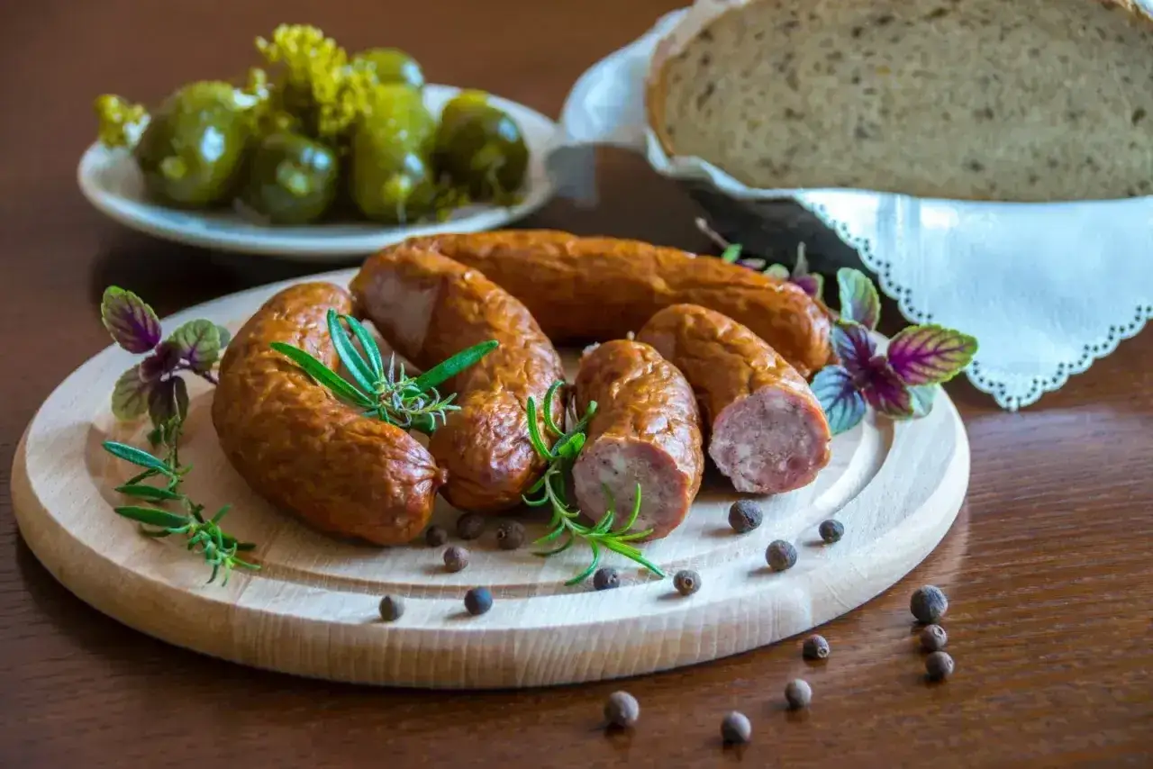 Wędzona kiełbasa na desce z ziołami i pieprzem. Idealna do chleba i ogórków. Zastanawiasz się, jaka sól do kiełbasy nada jej najlepszy smak?